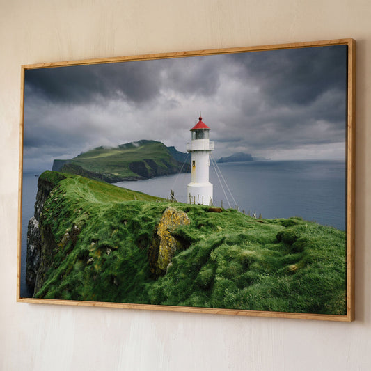 White Lighthouse on a Stormy Cliff, Coastal Canvas Wall Art shown in white oak floating frame