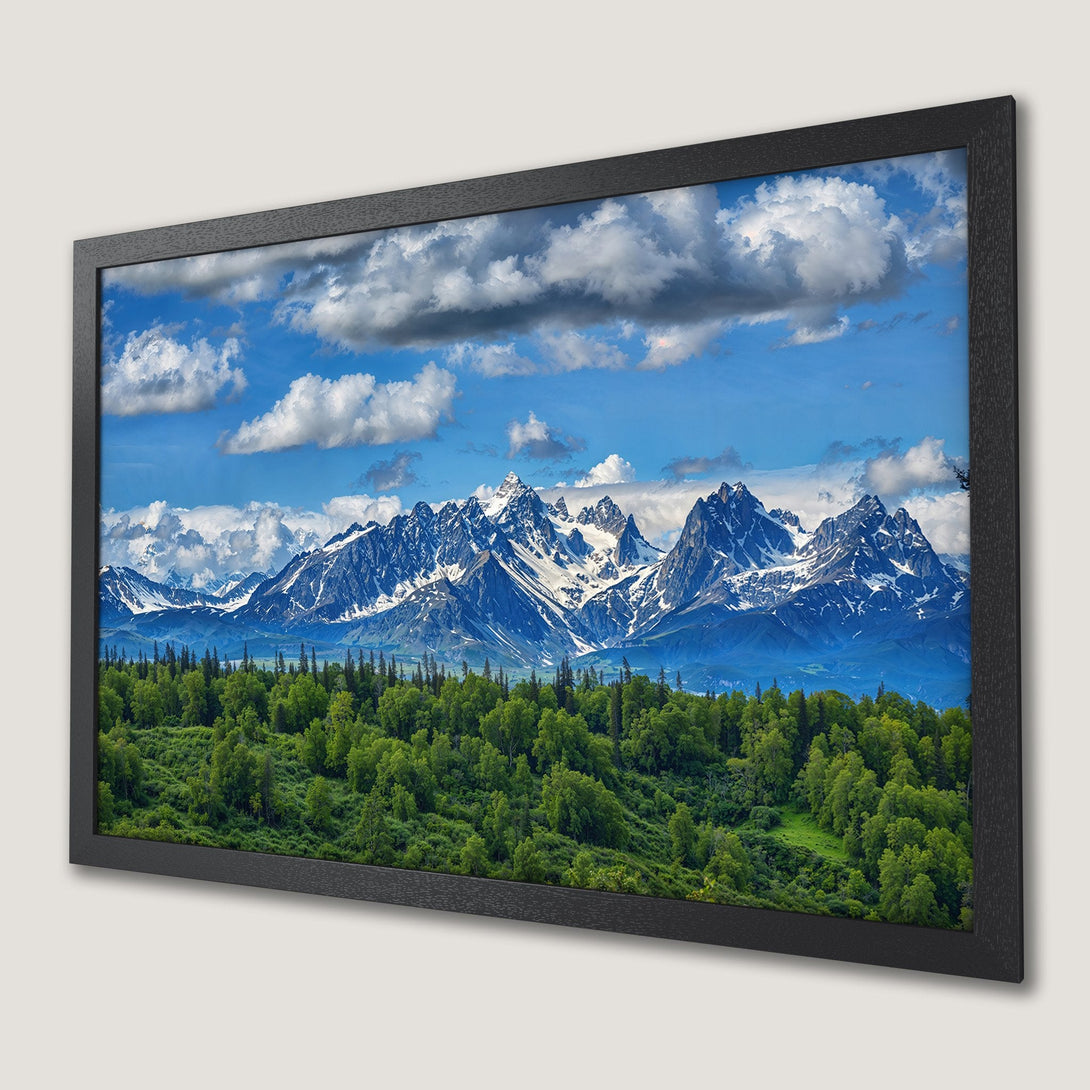 Framed Poster of majestic mountain landscape with vibrant green forest, blue sky, and white clouds. Perfect wall art!