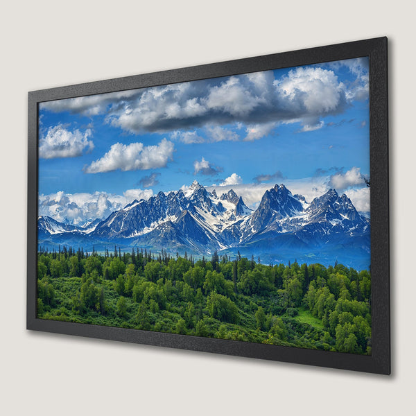Framed Poster of majestic mountain landscape with vibrant green forest, blue sky, and white clouds. Perfect wall art!