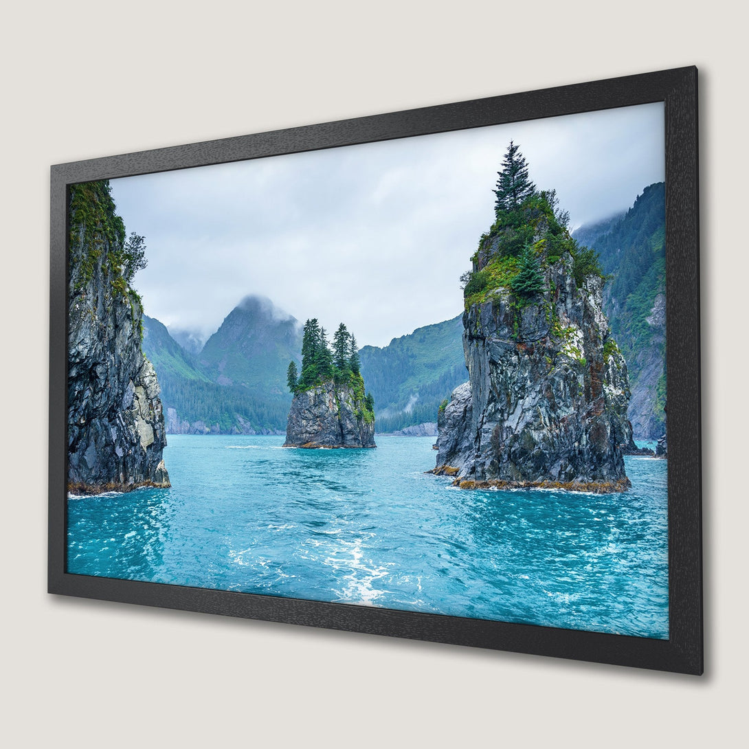 Framed Poster of serene coastal landscape with turquoise water, gray rocks, and green trees. Nature-inspired art in cool tones.