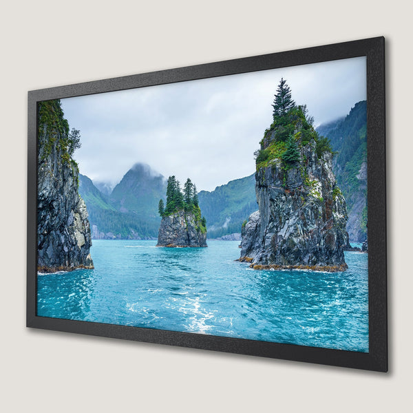 Framed Poster of serene coastal landscape with turquoise water, gray rocks, and green trees. Nature-inspired art in cool tones.