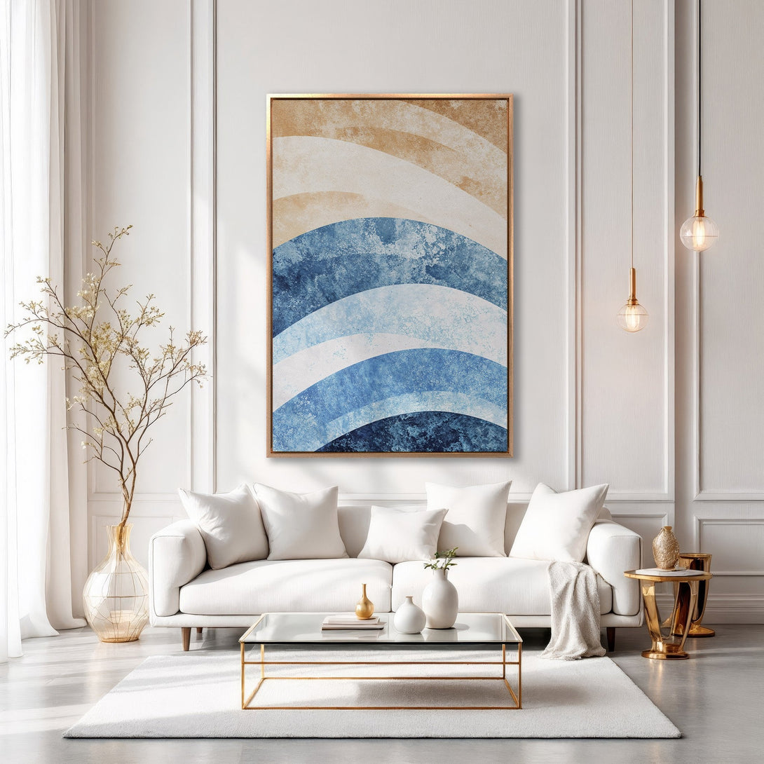 Framed Wall Art featuring abstract blue and beige waves. Modern style canvas print displayed in a chic living room with a neutral color palette.