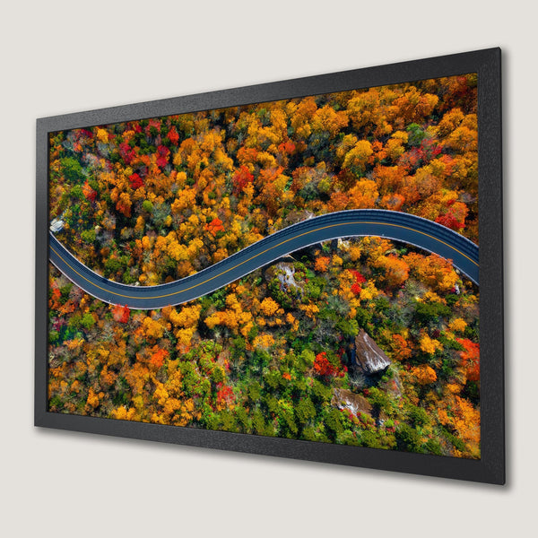 Framed Poster of winding road through vibrant autumn forest. Warm color palette with reds, oranges, and greens. Perfect wall art.