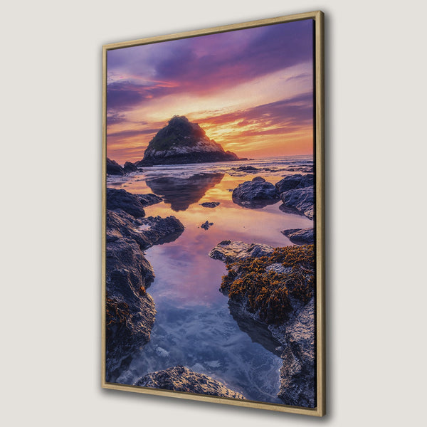 Framed Wall Art featuring a stunning sunset over a rocky coastline. Warm orange and purple hues create a serene landscape. Perfect for coastal decor!