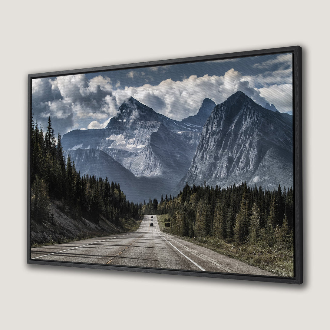 Framed Wall Art: Majestic mountain landscape Canvas Print. Serene road leads to towering peaks under a dramatic sky. Blue, green, and gray color palette.