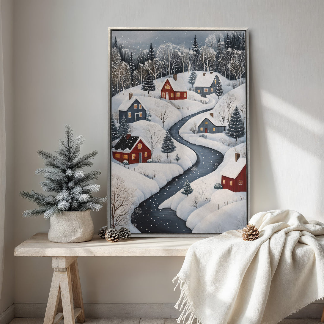 Framed Wall Art of a winter village scene. Cozy artwork with red houses, snow, and a river in a cool, muted color palette. Perfect for winter decor.