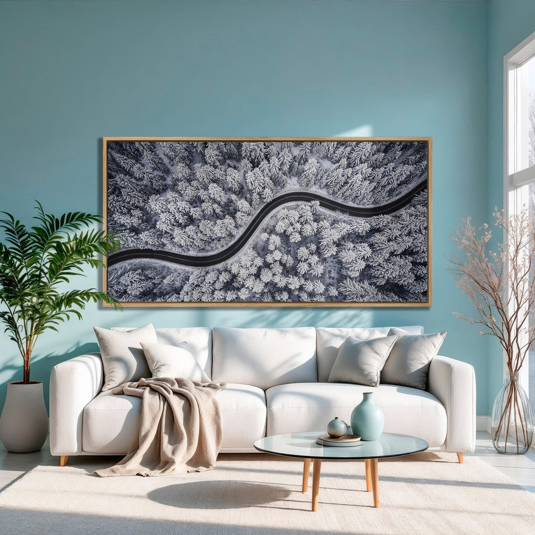 Framed Wall Art of a snowy forest road, displayed in a modern living room. Features a neutral color palette with pops of blue and white.