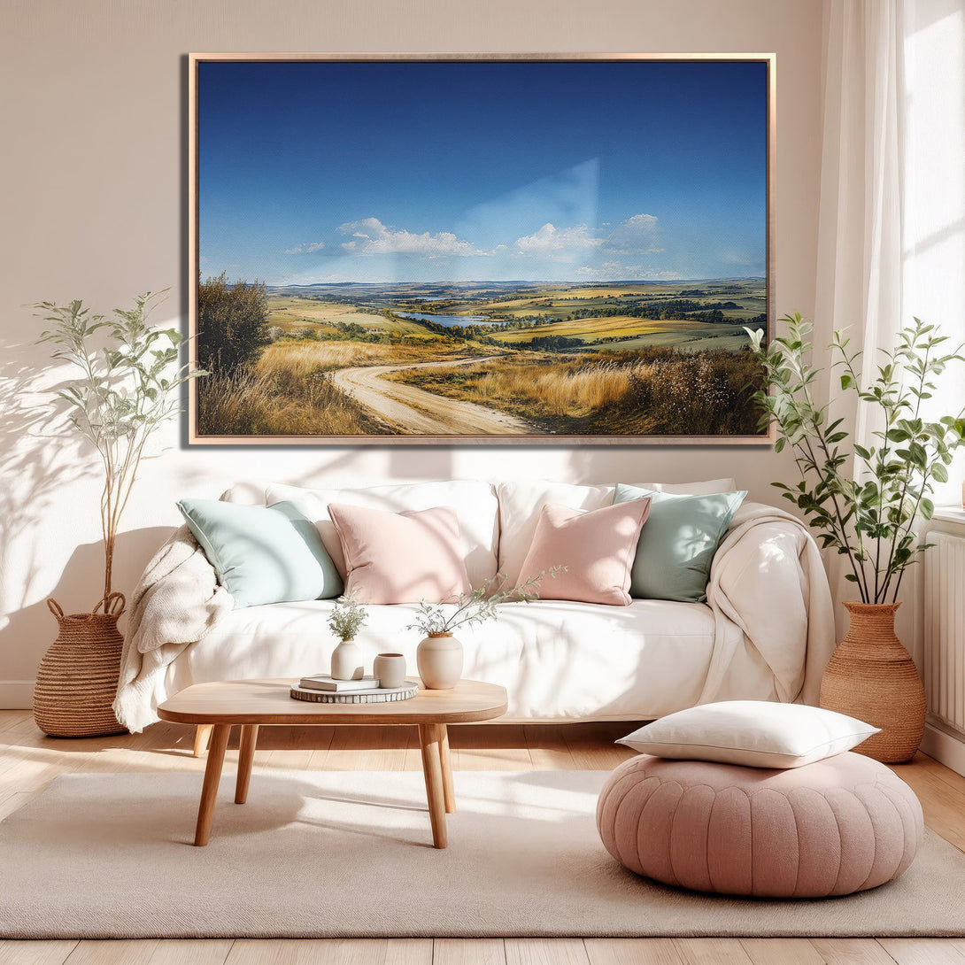 Framed Wall Art: Landscape Canvas Print in a warm, inviting living room. Features a scenic countryside view with blue sky, earth tones, and a touch of green.