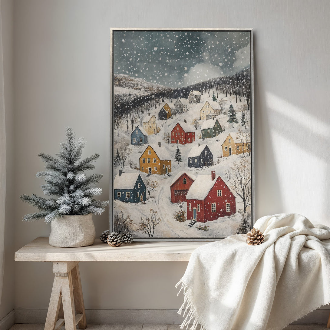 Framed Wall Art featuring a winter village scene in a cozy, folk art style. Warm, inviting color palette with pops of red, yellow, and blue. Perfect for holiday decor.