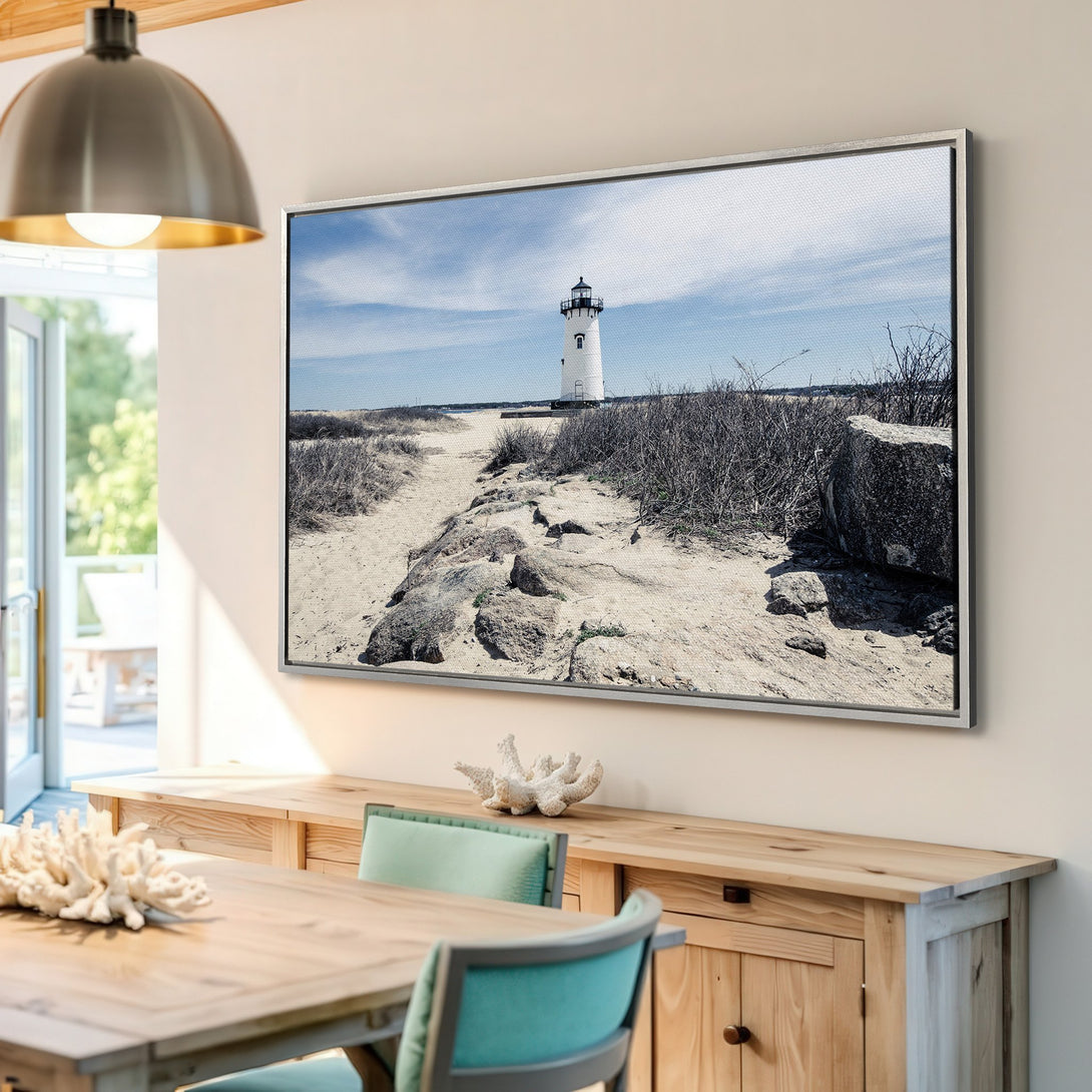 Framed Wall Art featuring a coastal lighthouse scene. Neutral color palette with blue sky and sandy tones. Coastal decor for a serene living space.
