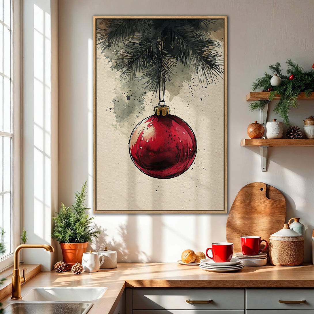Framed Wall Art: Watercolor Christmas ornament print in a warm kitchen. Features a vibrant red bauble, black branches, and neutral tones. Perfect holiday decor.