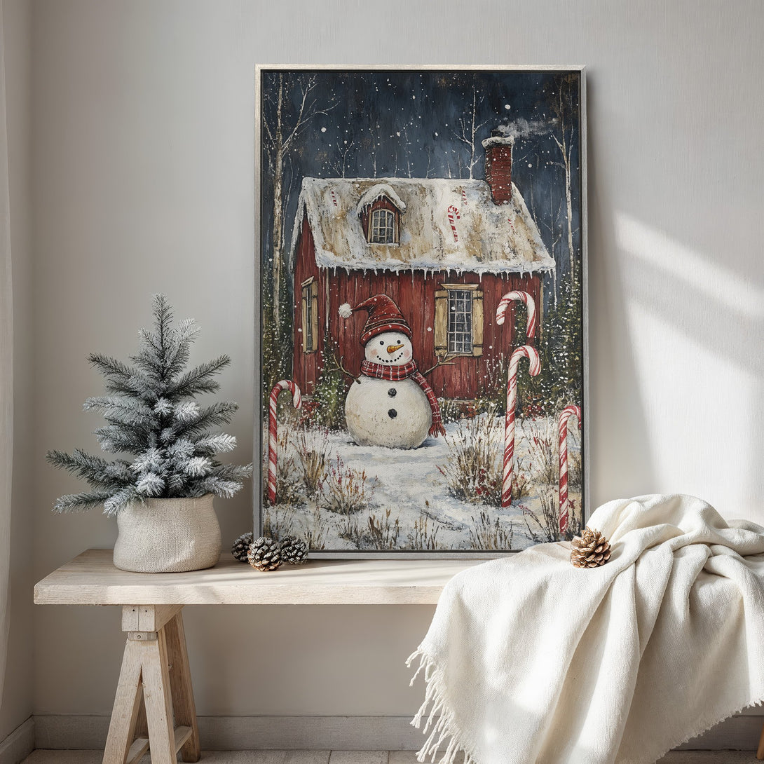 Framed Wall Art featuring a charming winter scene with a snowman and red cabin. Rustic style, warm red and white color palette. Perfect holiday decor.
