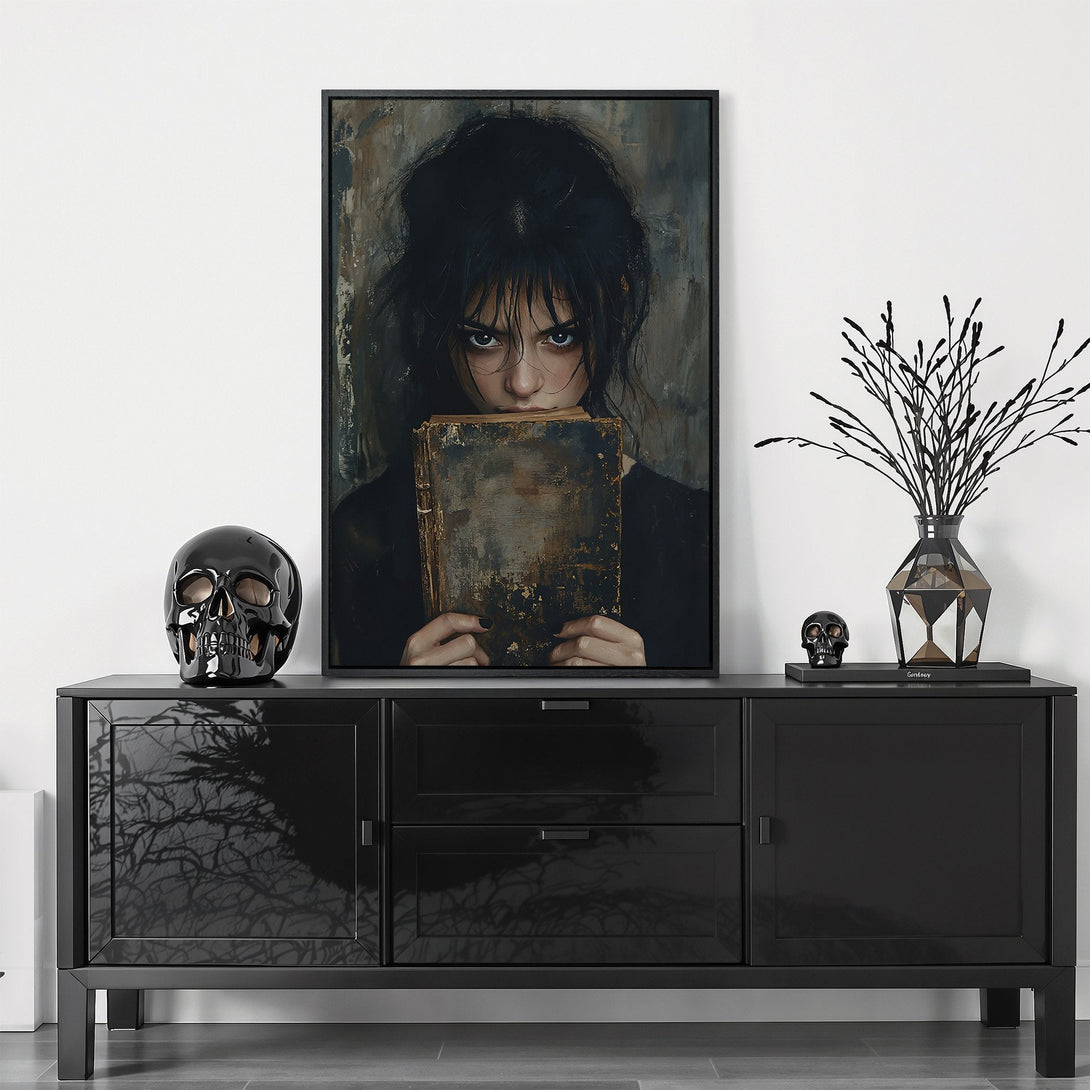 Framed Wall Art featuring a dark, moody portrait of a woman holding a book. Dramatic style with a muted, grayscale color palette. Perfect for adding a gothic touch.