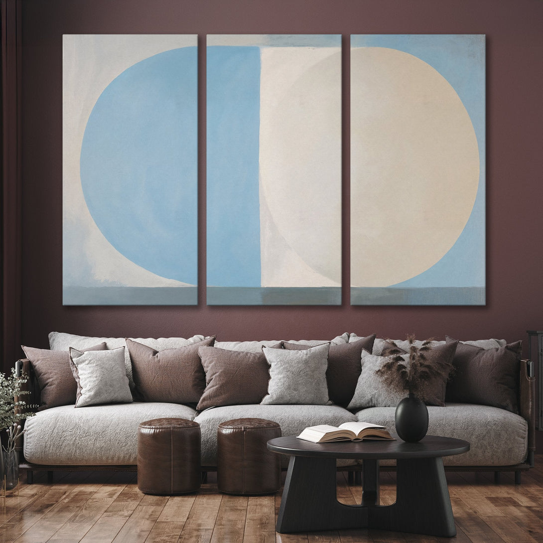Abstract Canvas Print triptych in blue and beige, displayed above a modern sofa. Adds a touch of calm sophistication to any space.