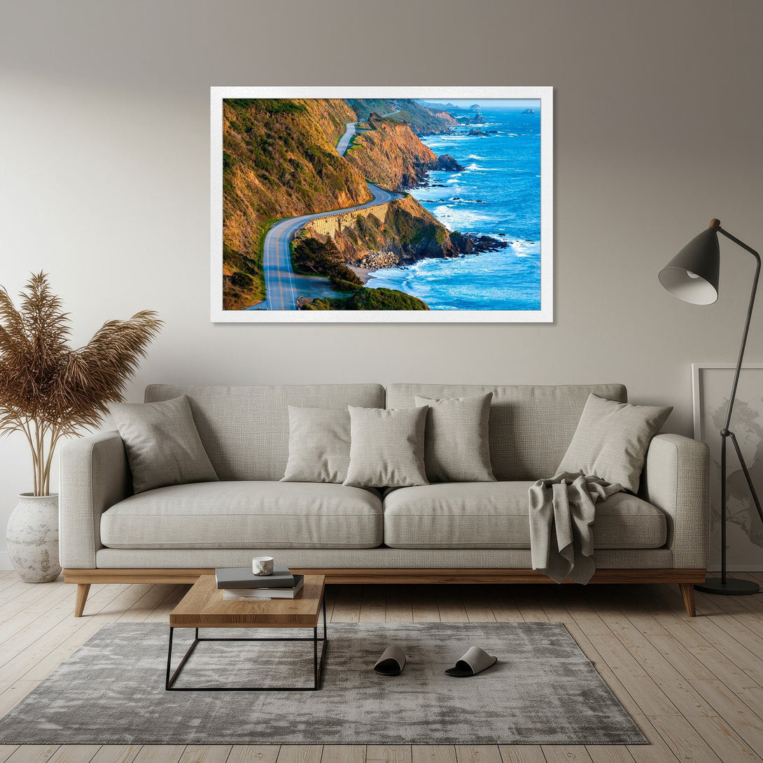 Framed Poster of scenic coastal highway. Featuring blue ocean, golden cliffs, and a vibrant color palette. Perfect wall art for your home!