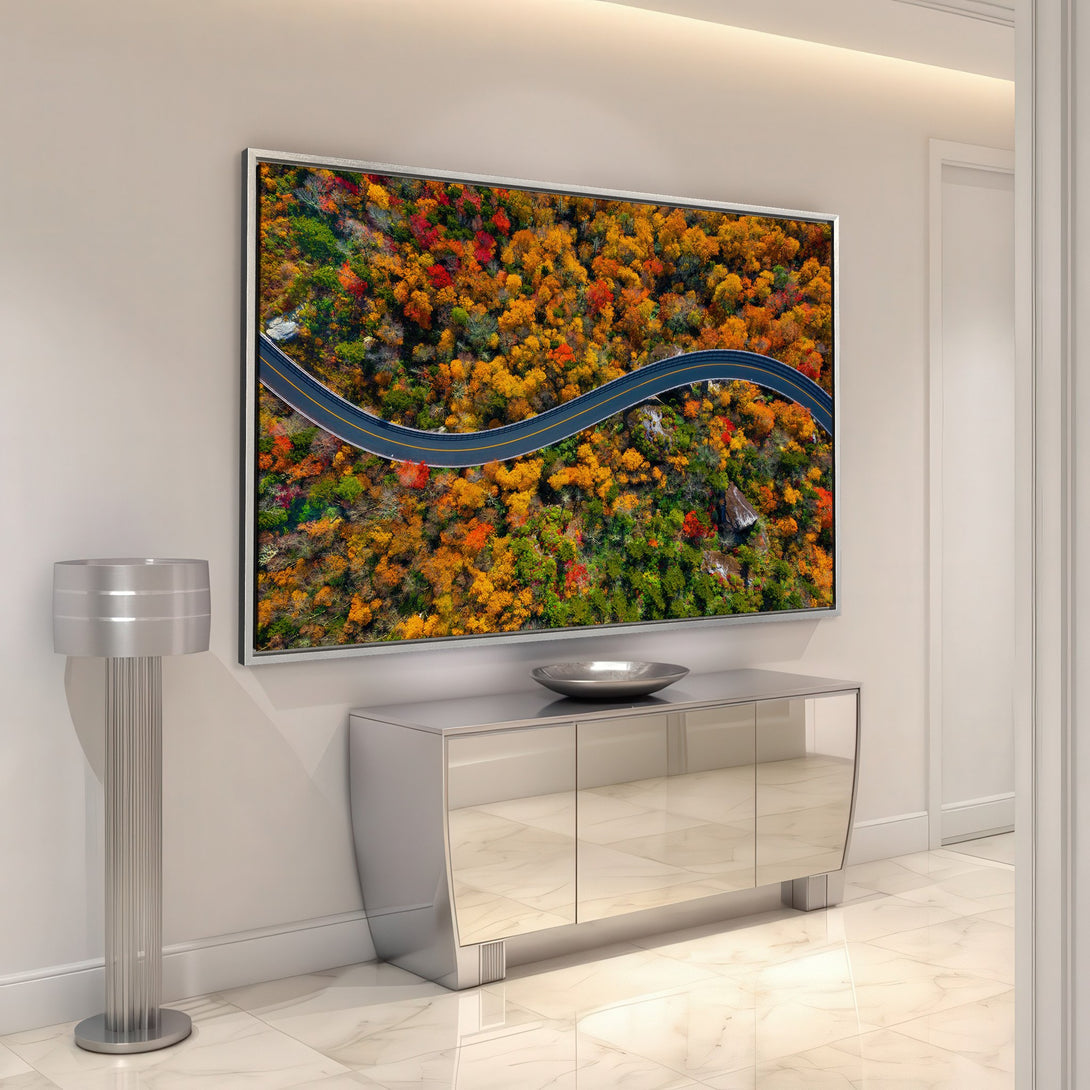 Framed Wall Art: Aerial view of a winding road through vibrant autumn trees. Warm, colorful palette of reds, oranges, and greens. Perfect for home decor!