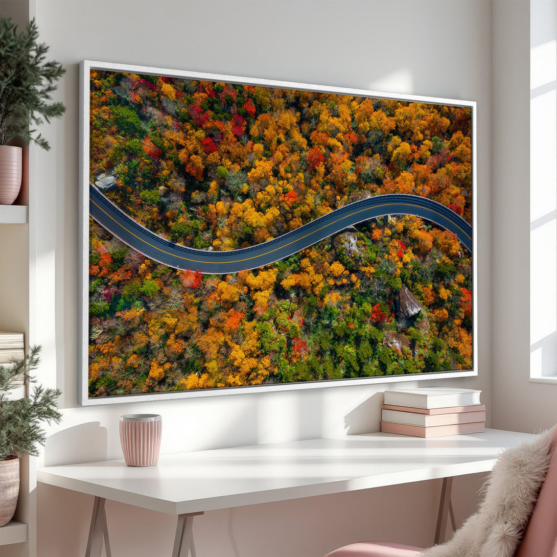 Framed Wall Art featuring an aerial view of a winding road through vibrant autumn foliage. Warm, colorful palette of reds, oranges, and greens. Perfect for home decor.