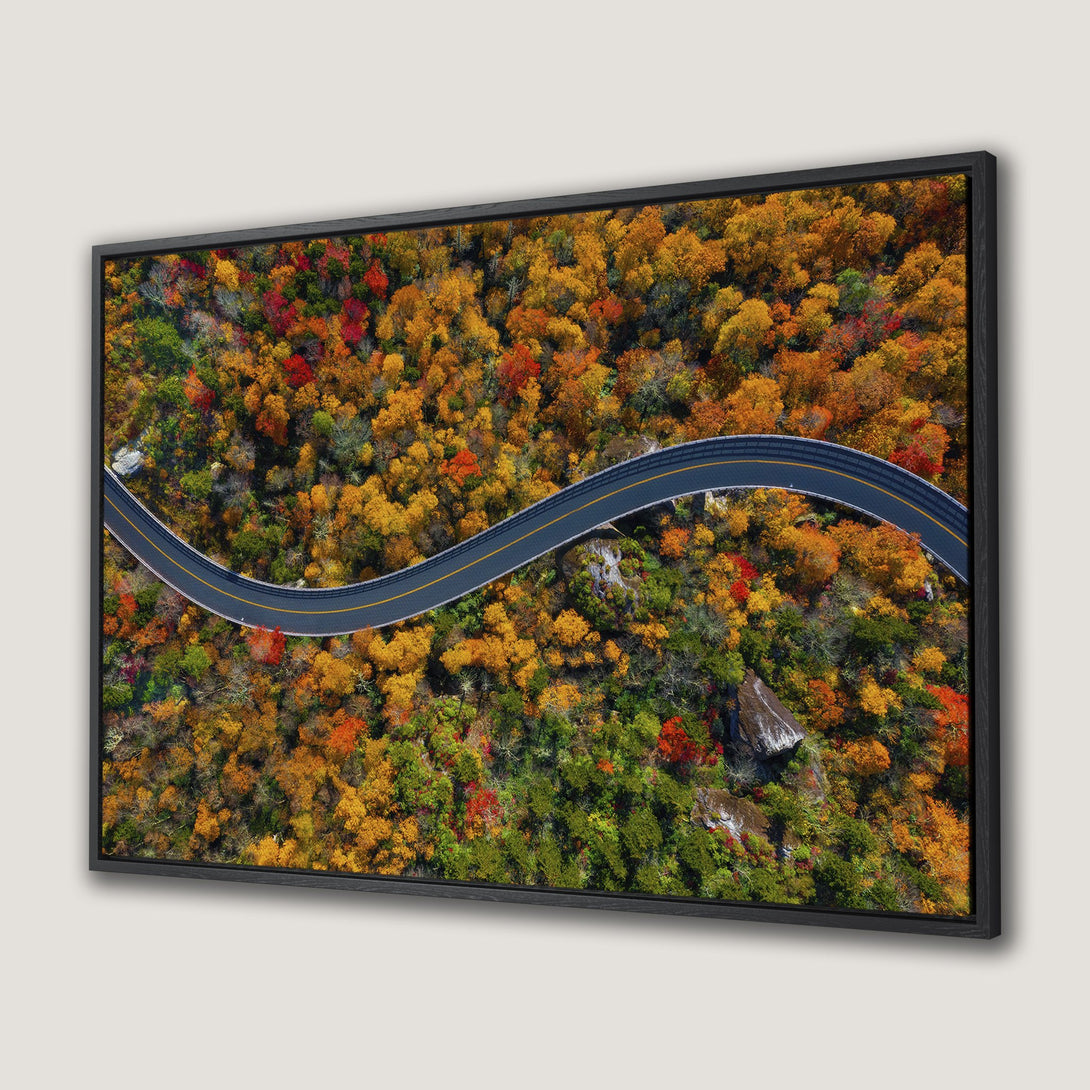 Framed Wall Art: Aerial view of a winding road through vibrant autumn trees in orange, yellow, and red hues. Stunning landscape Canvas Print.
