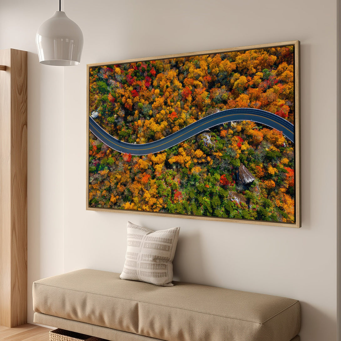 Framed Wall Art: Aerial view of a winding road through vibrant autumn forest. Warm color palette of reds, oranges, and greens. Perfect for home decor.