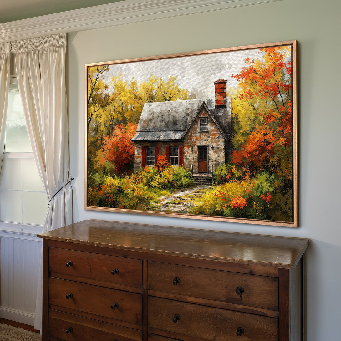 Framed Wall Art featuring a cozy cottage in an autumn landscape. Warm color palette of reds, oranges, and yellows, perfect for home decor.