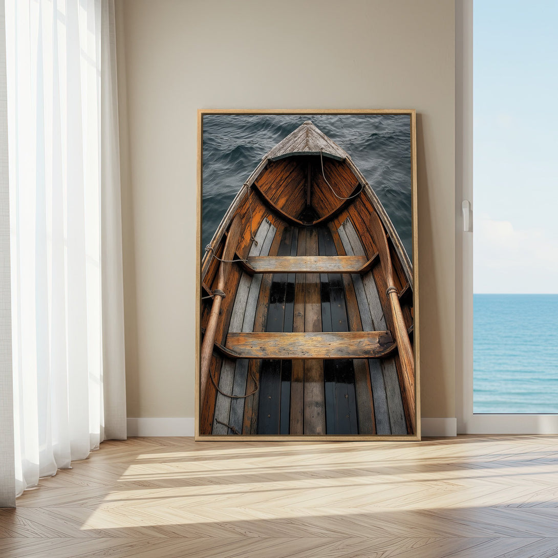 Framed Wall Art of a rustic wooden boat on the water, displayed in a bright room. Coastal style with warm wood and cool blue tones.