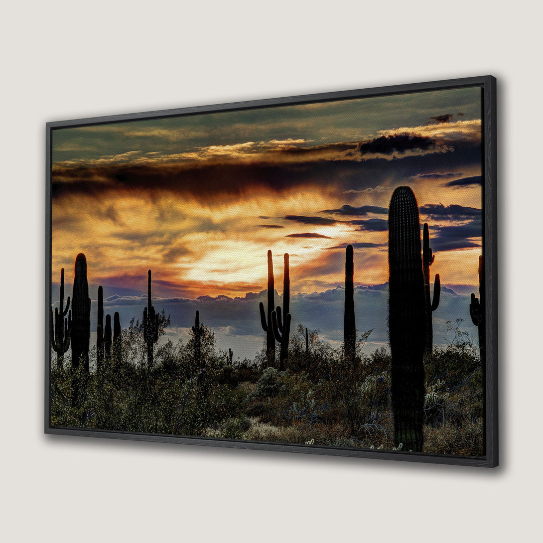 Framed Wall Art of a desert sunset with silhouetted cacti. Warm orange and gold hues paint the sky, creating a southwestern style aesthetic.
