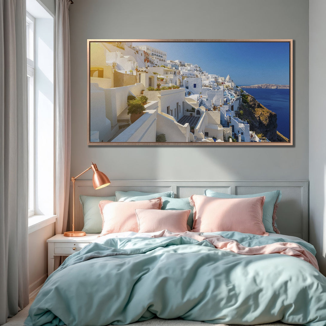 Framed Wall Art of Santorini village in a bedroom. Coastal decor with white buildings, blue sea, and a calming pastel color palette.