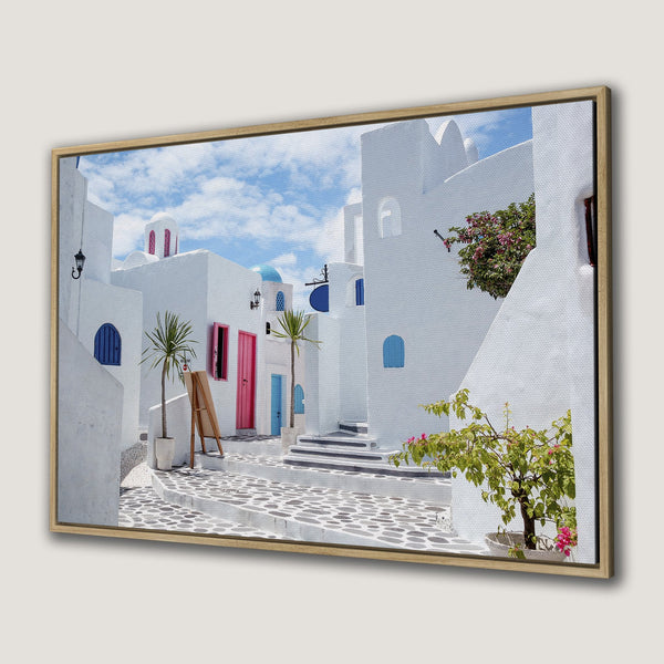 Canvas Print of a charming Greek village scene, featuring white buildings, blue accents, and a vibrant pink and blue color palette.