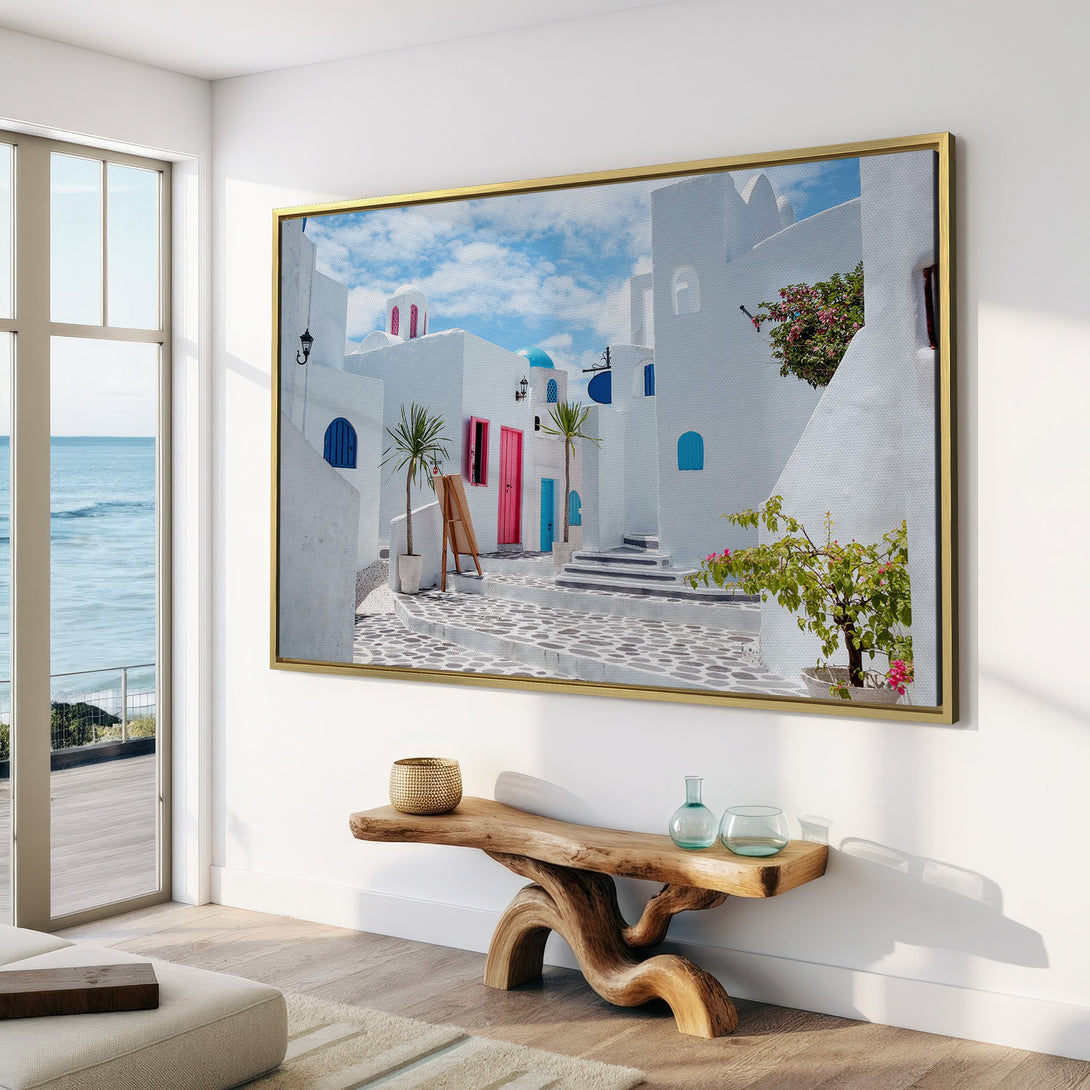 Canvas Print of a Greek village scene. White buildings with blue accents and pink doors. Coastal style art with a bright, airy color palette.