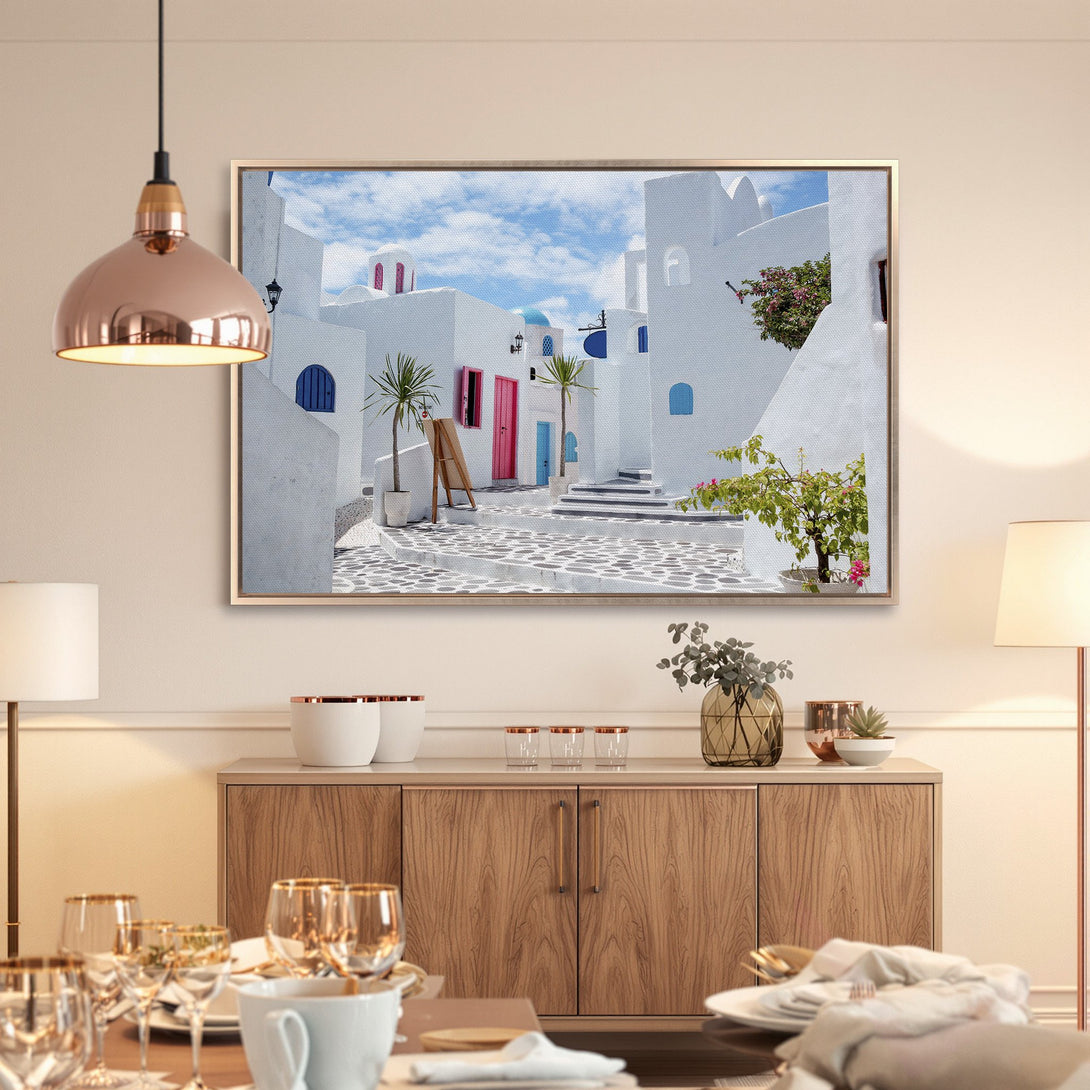 Framed Wall Art featuring a picturesque Greek village scene. White buildings, blue accents, & pops of pink. Bring Mediterranean vibes to your home!