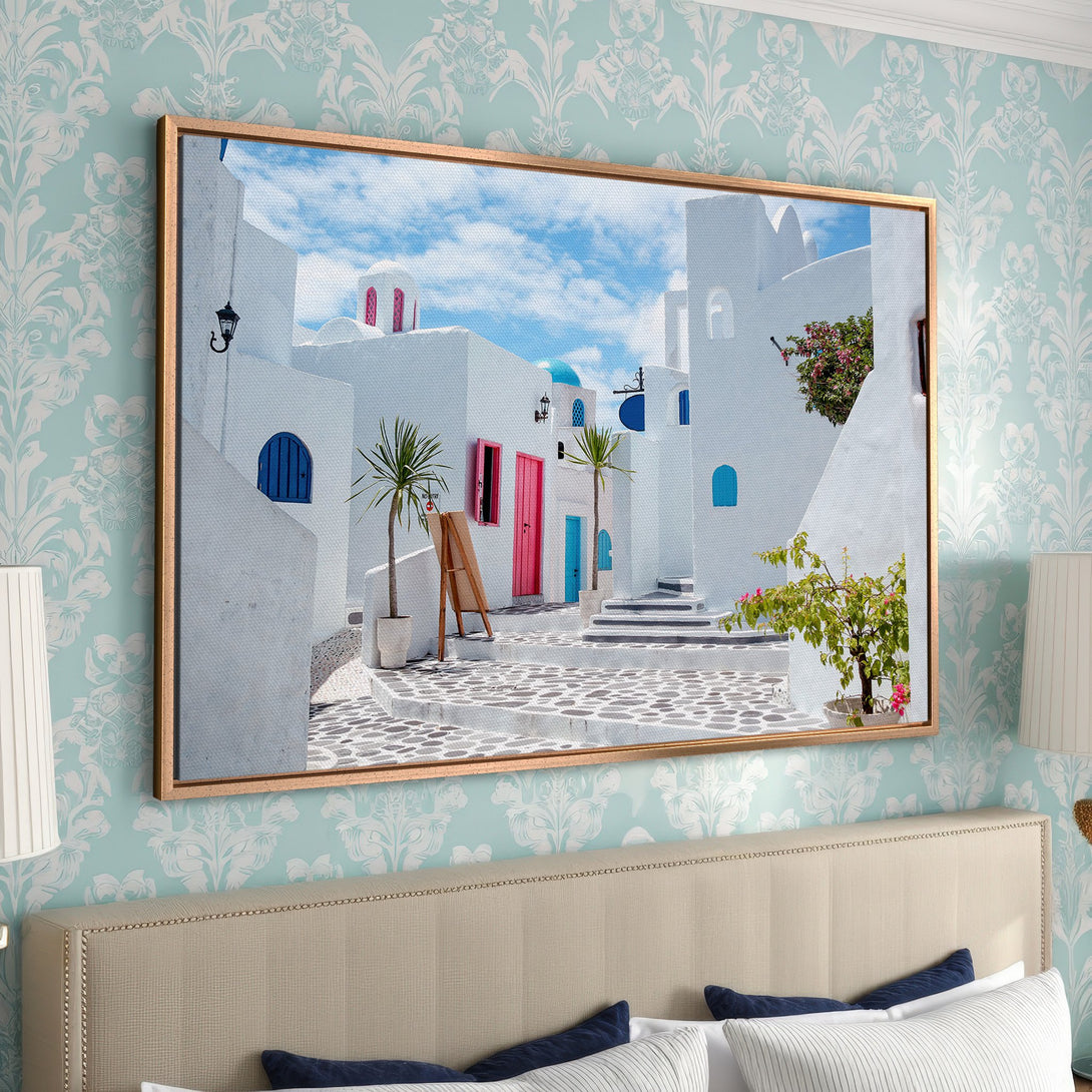 Framed Wall Art of a Santorini scene with white buildings, blue accents, and pink doors. Coastal style canvas print with a vibrant color palette.