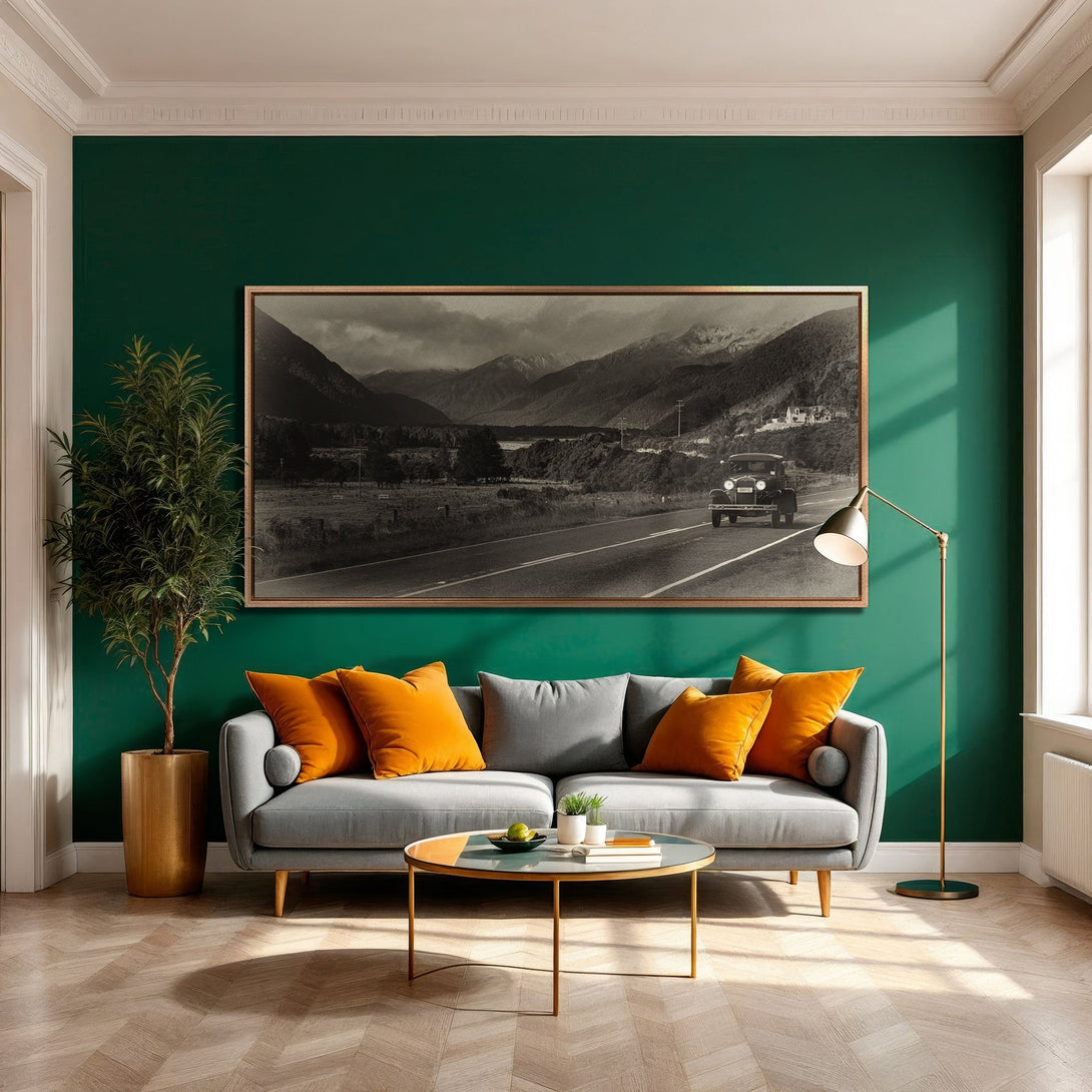 Framed Wall Art featuring a vintage car on a mountain road. Stylish black and white print with a gold frame, set in a modern interior with green and orange accents.