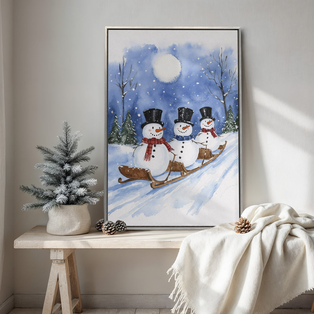 Framed Wall Art featuring a watercolor painting of snowmen sledding in a winter scene. Blue, white, and brown color palette. Perfect for holiday decor!