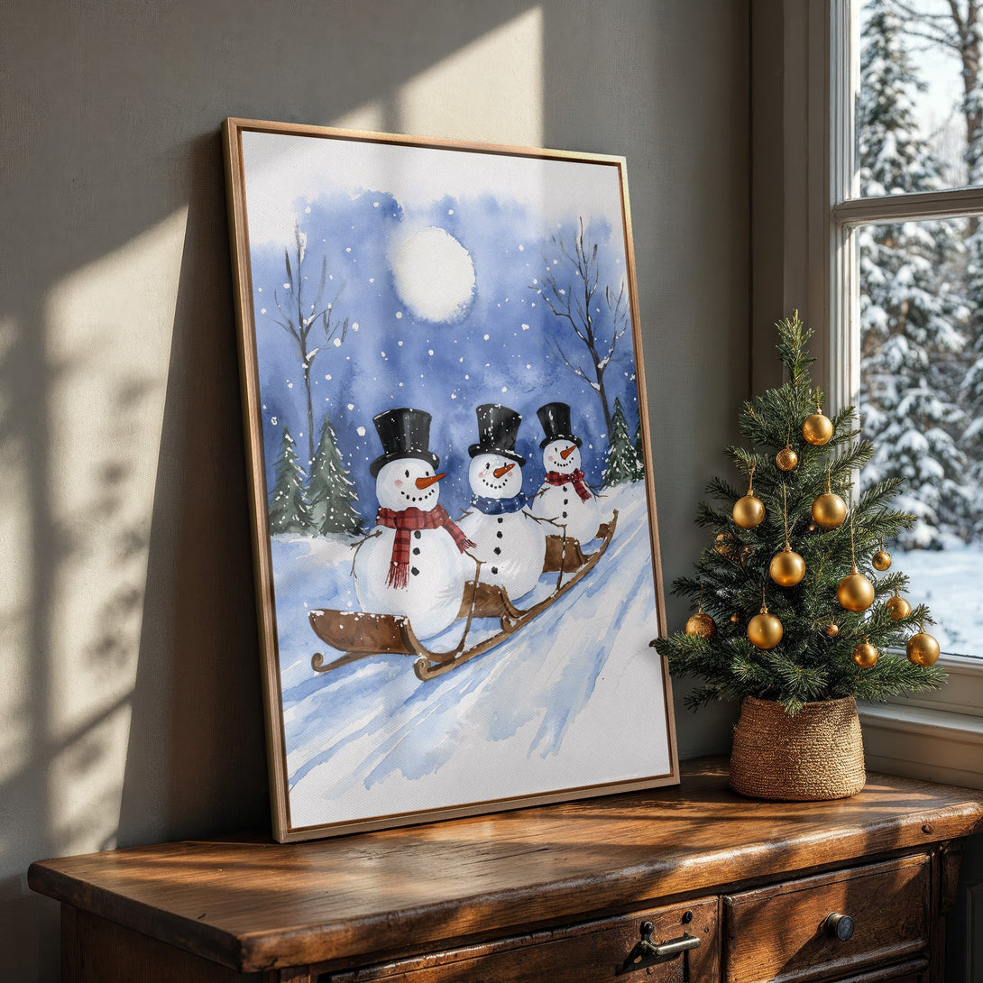 Framed Wall Art featuring watercolor snowmen on a sled, perfect for winter decor. Blue and white color palette adds a cozy, festive touch to any room.