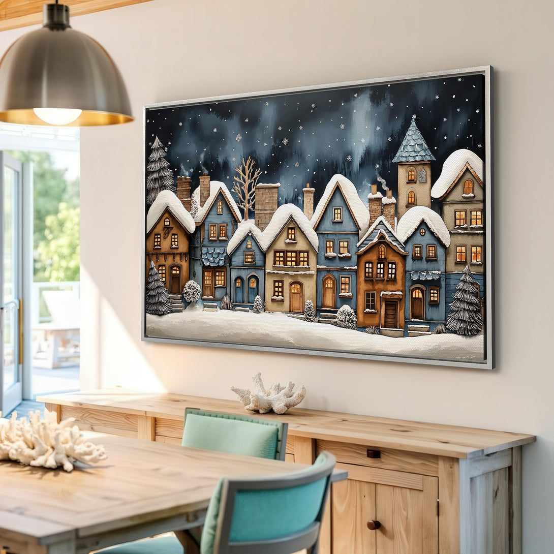 Framed Wall Art featuring a charming winter village scene with snow-covered houses. Warm, cozy colors in a whimsical style. Perfect for adding a touch of holiday cheer.